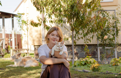 Woman holding her cat in the garden with her dog resting behind