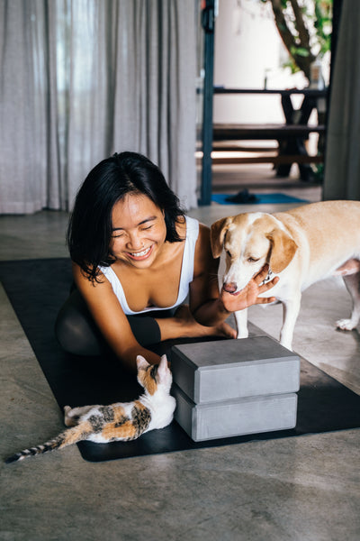Woman laughing on a yoga mat with her dog and kitten